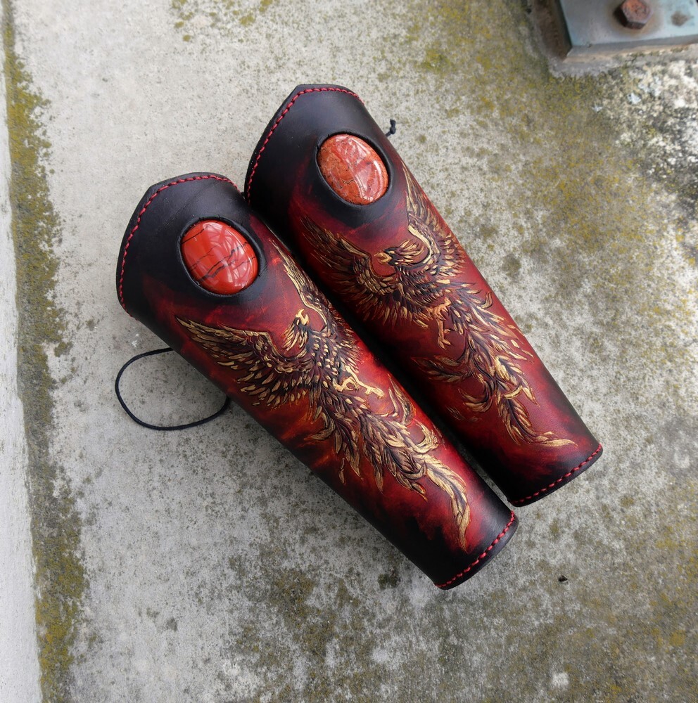 Paire de brassards sur un fond gris représentant des phénix dorés, rouge et noirs avec une inclusion de jaspe rouge au dessus 