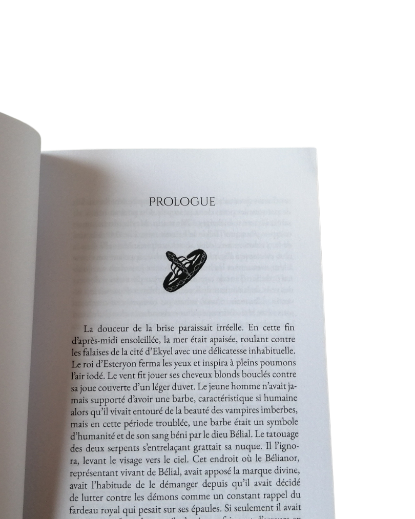 PROLOGUE La douceur de la brise paraissait En cette fin d'après-midi ensoleillée, la mer était apaisée, roulant contre les falaises de la cité d'Ekyel avec une délicatesse inhabituelle. Le roi d'Esteryon ferma les yeux et inspira à pleins poumons l'air iodé. Le vent fit jouer ses cheveux blonds contre sa joue couverte d'un léger duvet. Le jeune homme n'avait ja- mais supporté d'avoir une barbe, caractéristique si humaine alors qu'il vivait entouré de la beauté des vampires imberbes, mais en cette période troublée, une barbe était un symbole d'humanité et de son sang béni par le dieu Bélial. Le tatouage des deux serpents s'entrelaçant grattait sa nuque. Il l'igno- ra, levant le visage vers le ciel. Cet endroit où le Bélianor, représentant vivant de Bélial, avait apposé la marque divine, avait l'habitude de le démanger depuis qu'il avait décidé de lutter contre les démons comme un constant rappel du fardeau royal qui pesait sur ses épaules. Si seulement il avait